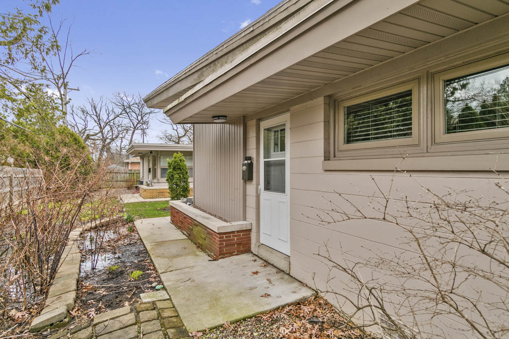 A modern, minimally furnished room with a window, featuring a beige armchair, matching blanket, bookshelf, and small coffe...