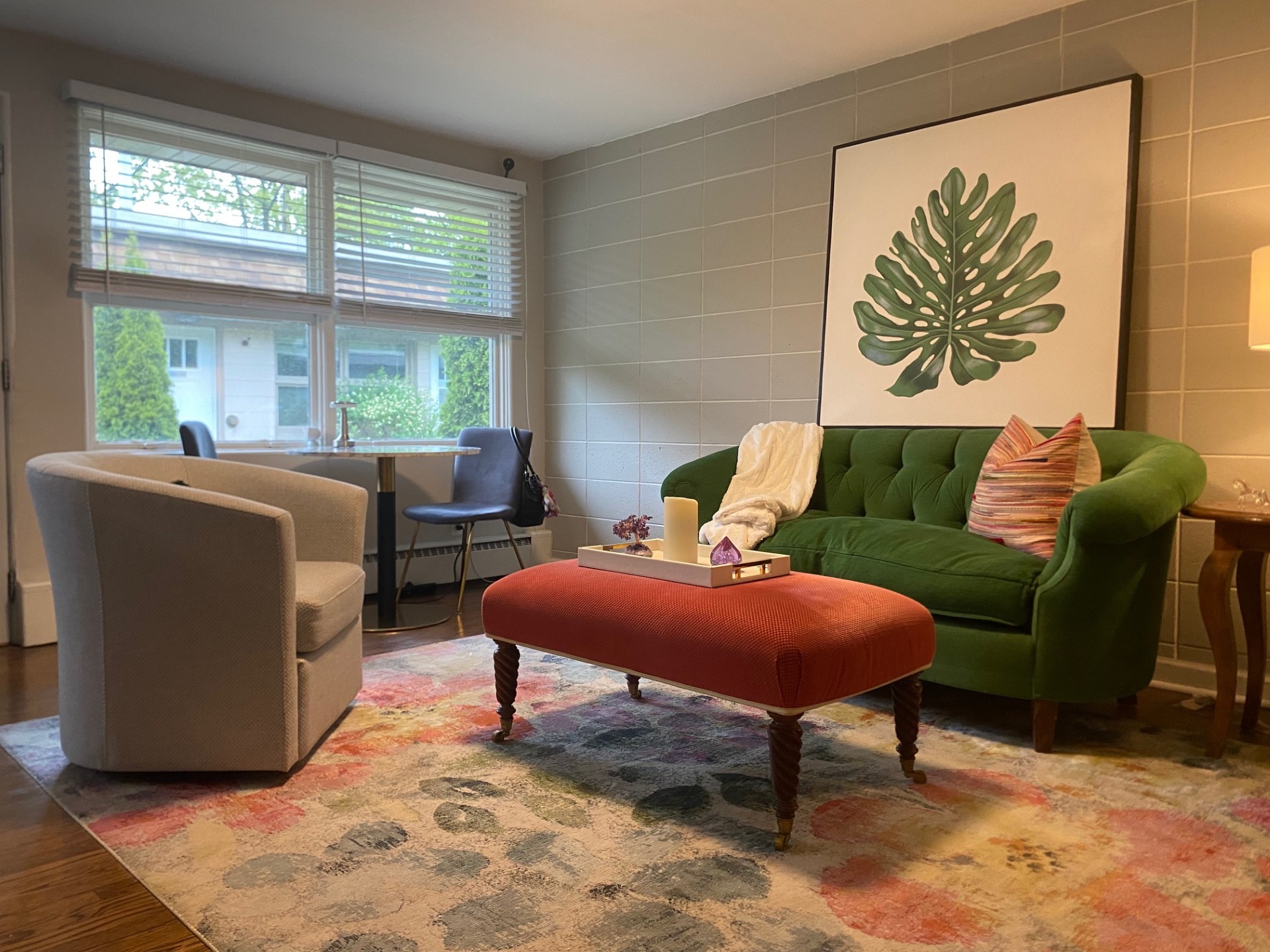 A modern, minimally furnished room with a window, featuring a beige armchair, matching blanket, bookshelf, and small coffe...